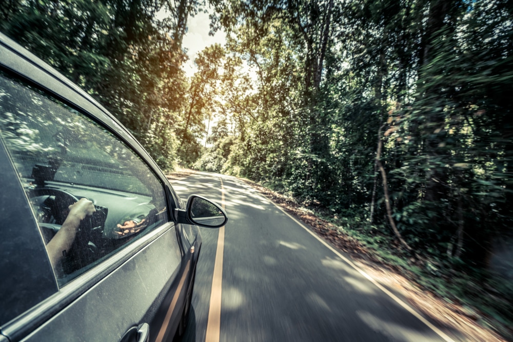 Side view of black car driving on road in forest highway in summer. Travel and explore concept.